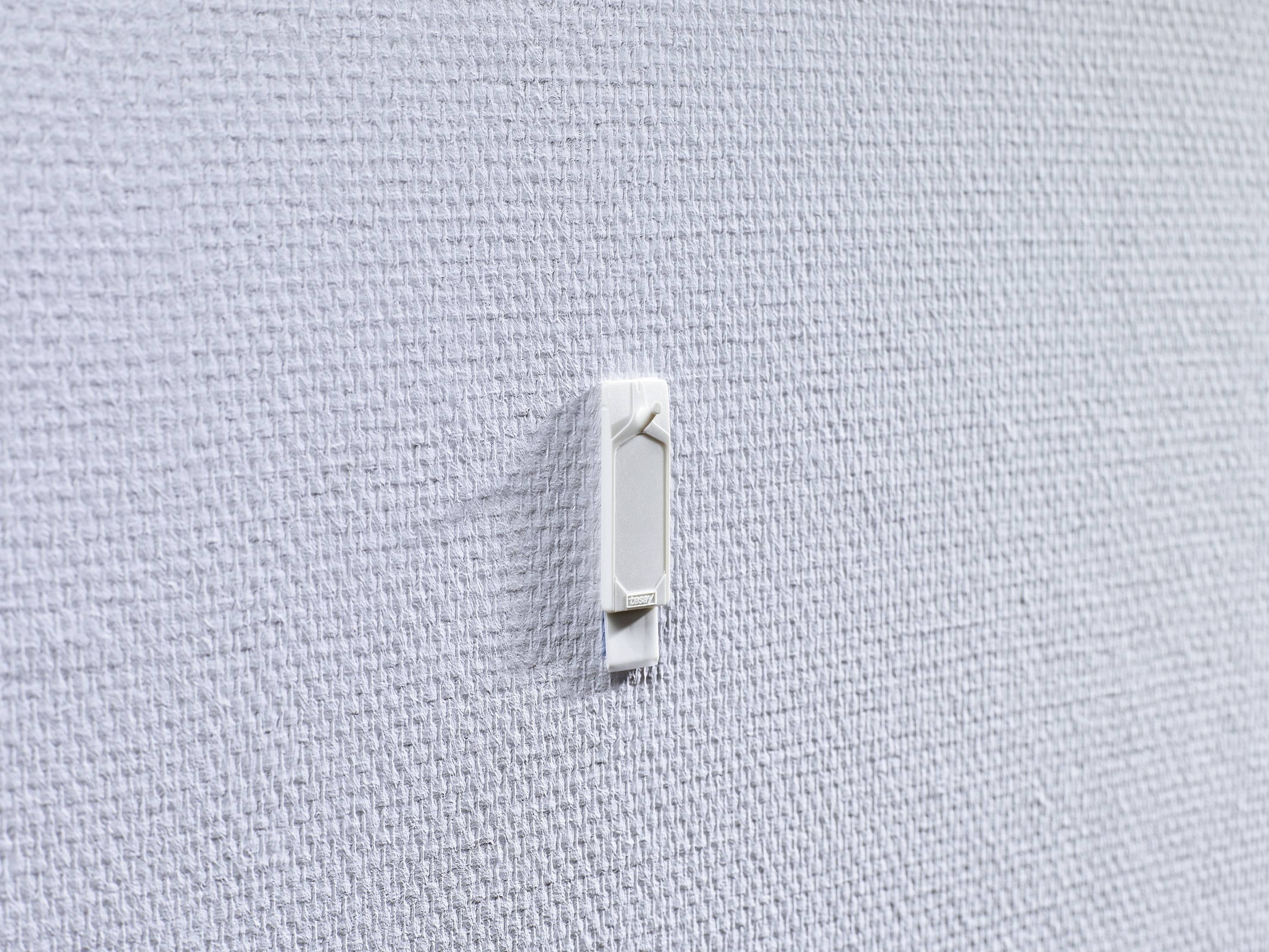 Weißer Kunststoffclip an einer strukturierten, grauen Wandoberfläche befestigt.