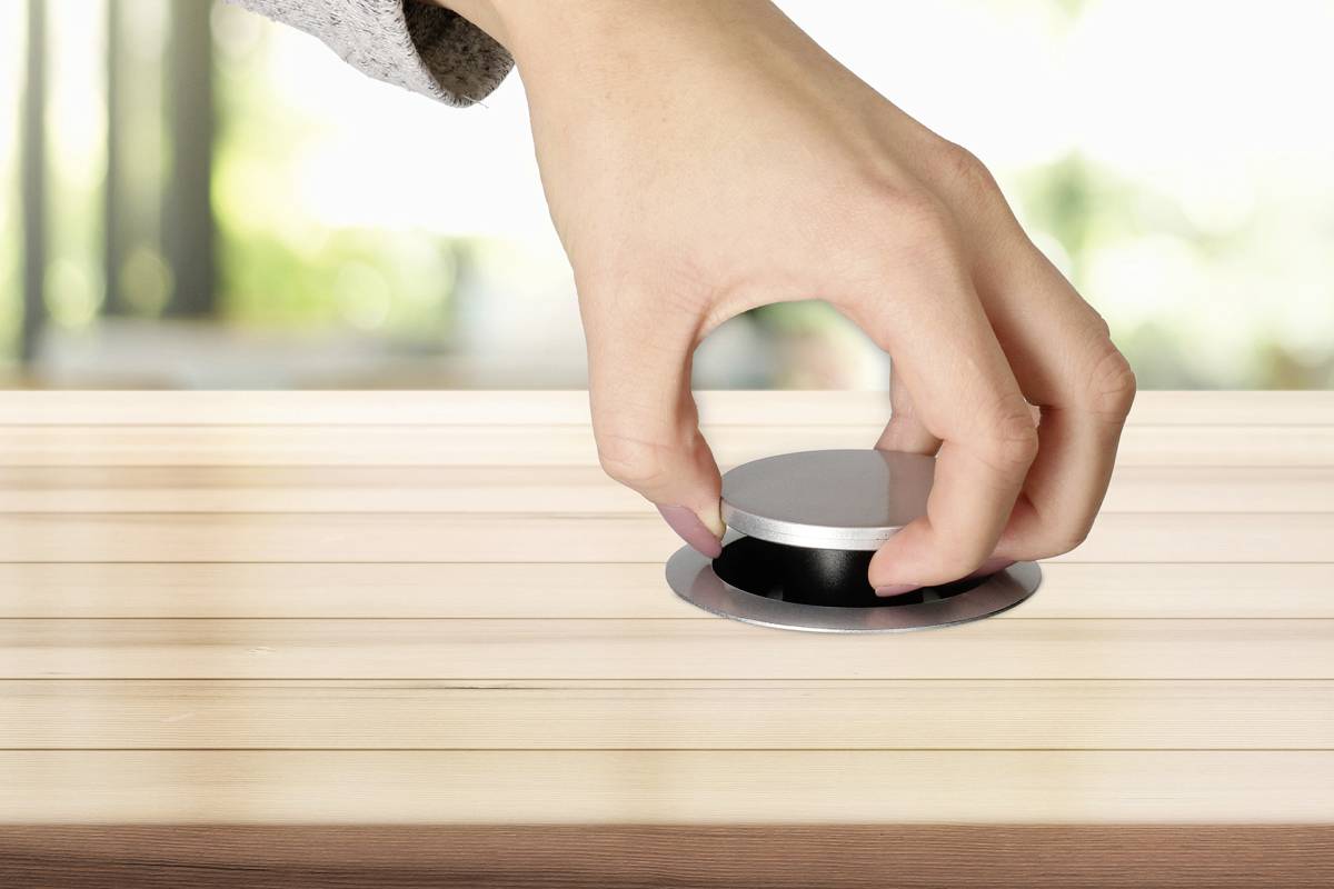 Eine Hand zieht einen runden, versenkbaren Knopf aus einer Holzoberfläche heraus.