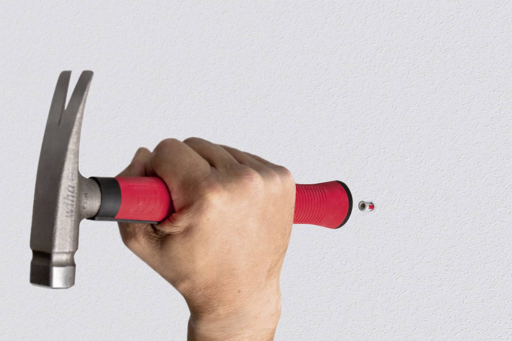Eine Hand hält einen Hammer mit rotem Griff und schlägt einen Nagel in die Wand. Der Hintergrund ist grau.