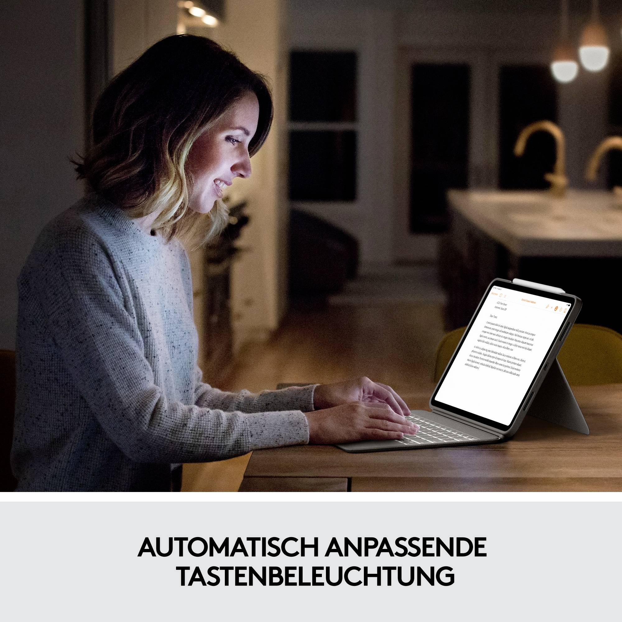 Frau sitzt an einem Tisch und benutzt ein Tablet mit leuchtender Tastatur in dunkler Umgebung. Text im Bild: 'Automatisch anpassende Tastenbeleuchtung'.