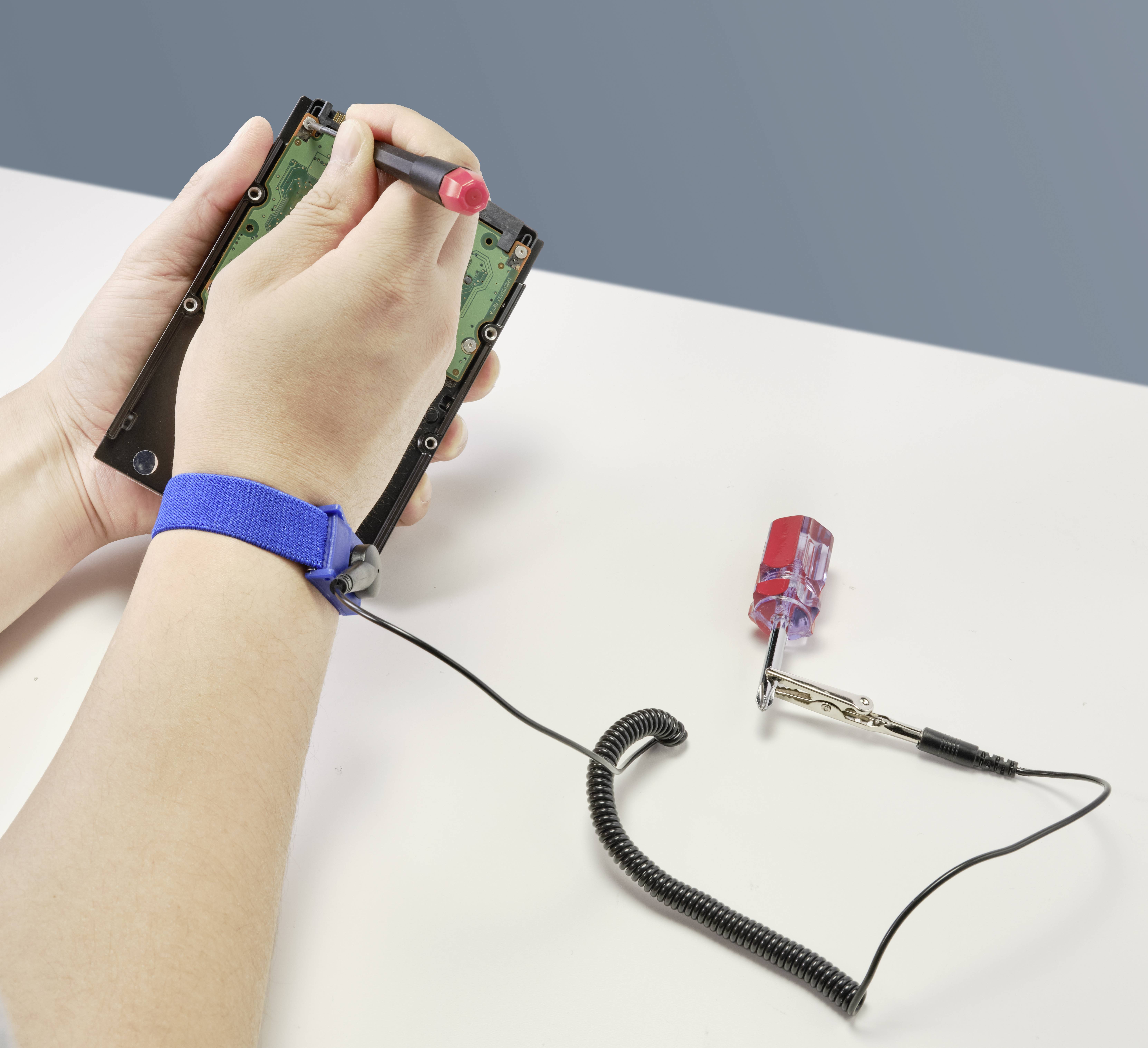 Eine Person hält eine Festplatte und arbeitet daran mit einem Schraubendreher. Ein Erdungsarmband ist am Handgelenk befestigt.