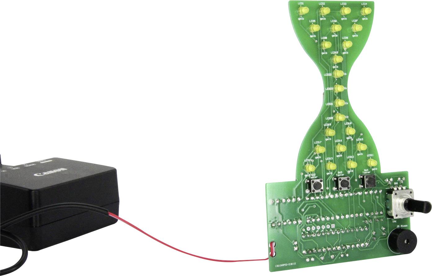 'Electronisches Spielzeug' zeigt ein grünes Schaltbrett mit LEDs, Tasten und einem Drehschalter, verbunden mit einem schwarzen Batteriefach.