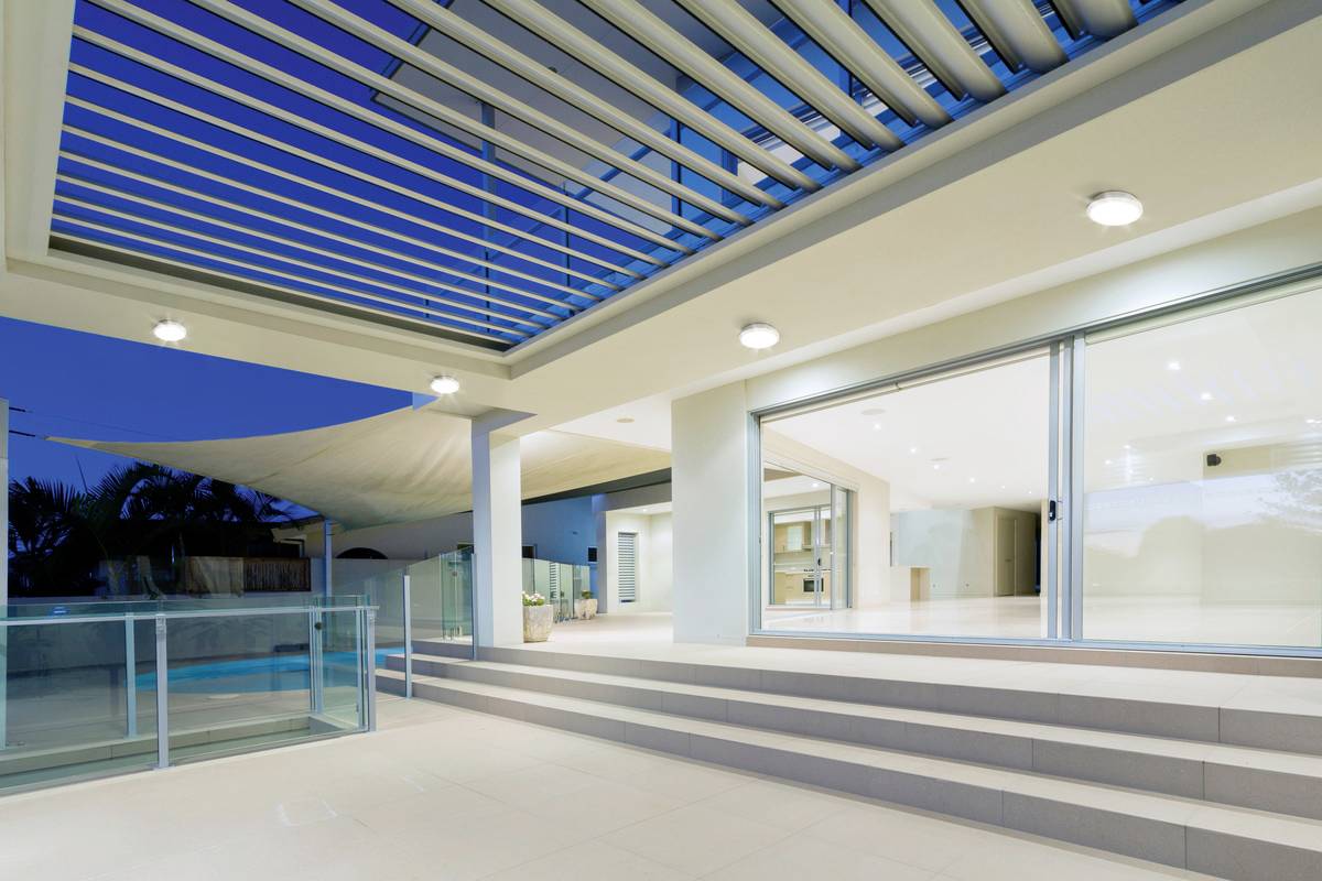 Ein modernes Gebäude mit großem, offenen Terrassenbereich, beleuchtet bei Dämmerung. Glasschiebetüren führen ins Innere.