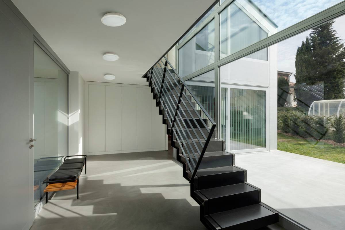 Innenraum mit moderner Treppe, großen Glasfronten und direktem Blick auf einen Garten, der viel Tageslicht einlässt.