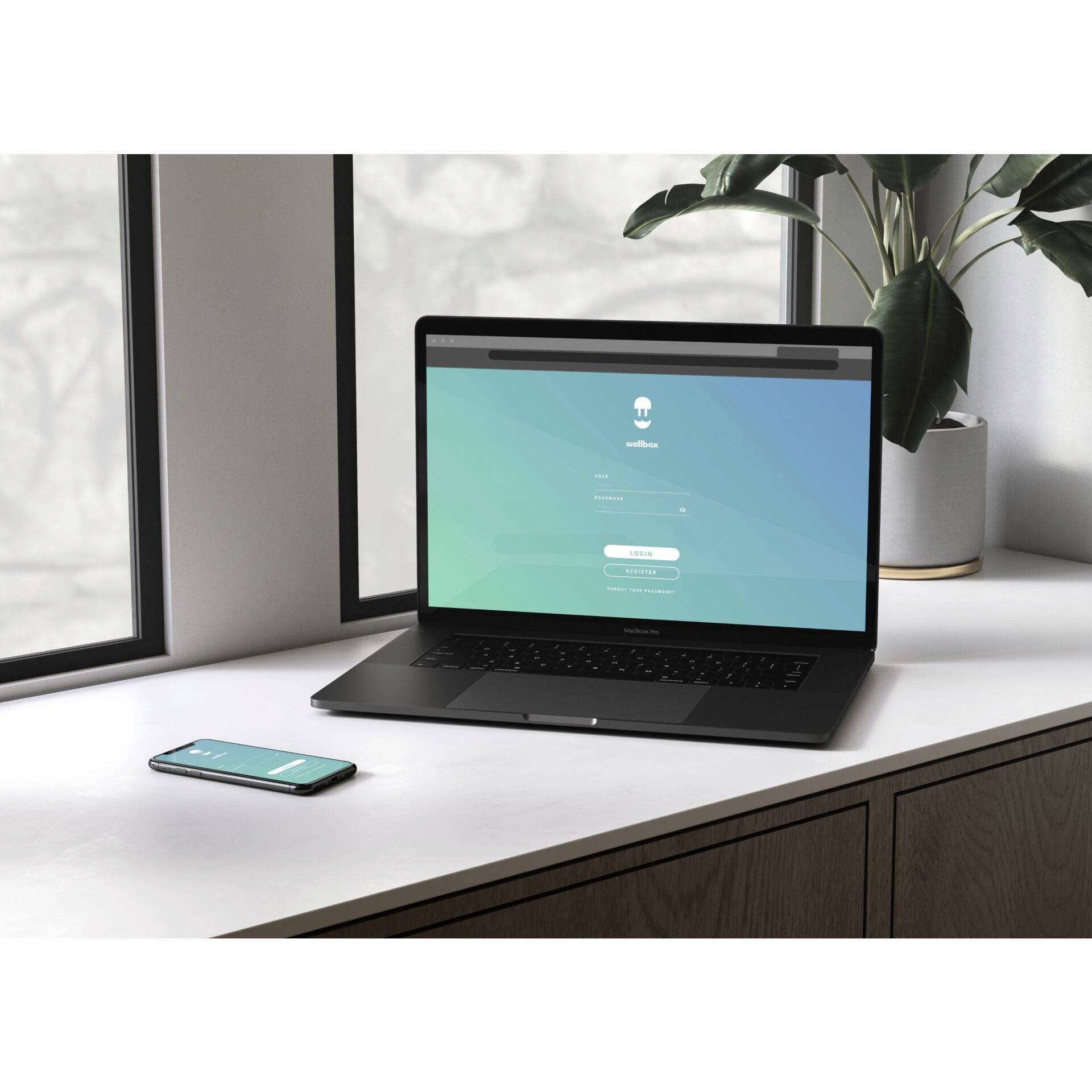 Ein Laptop zeigt einen Anmeldebildschirm mit grünem Hintergrund. Daneben liegt ein Smartphone auf einem Tisch neben einem Fenster.