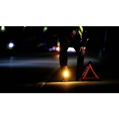 Eine Person platziert nachts ein leuchtendes Warnsignal und ein Warndreieck auf der Straße, um vor einem potenziellen Unfall zu warnen.