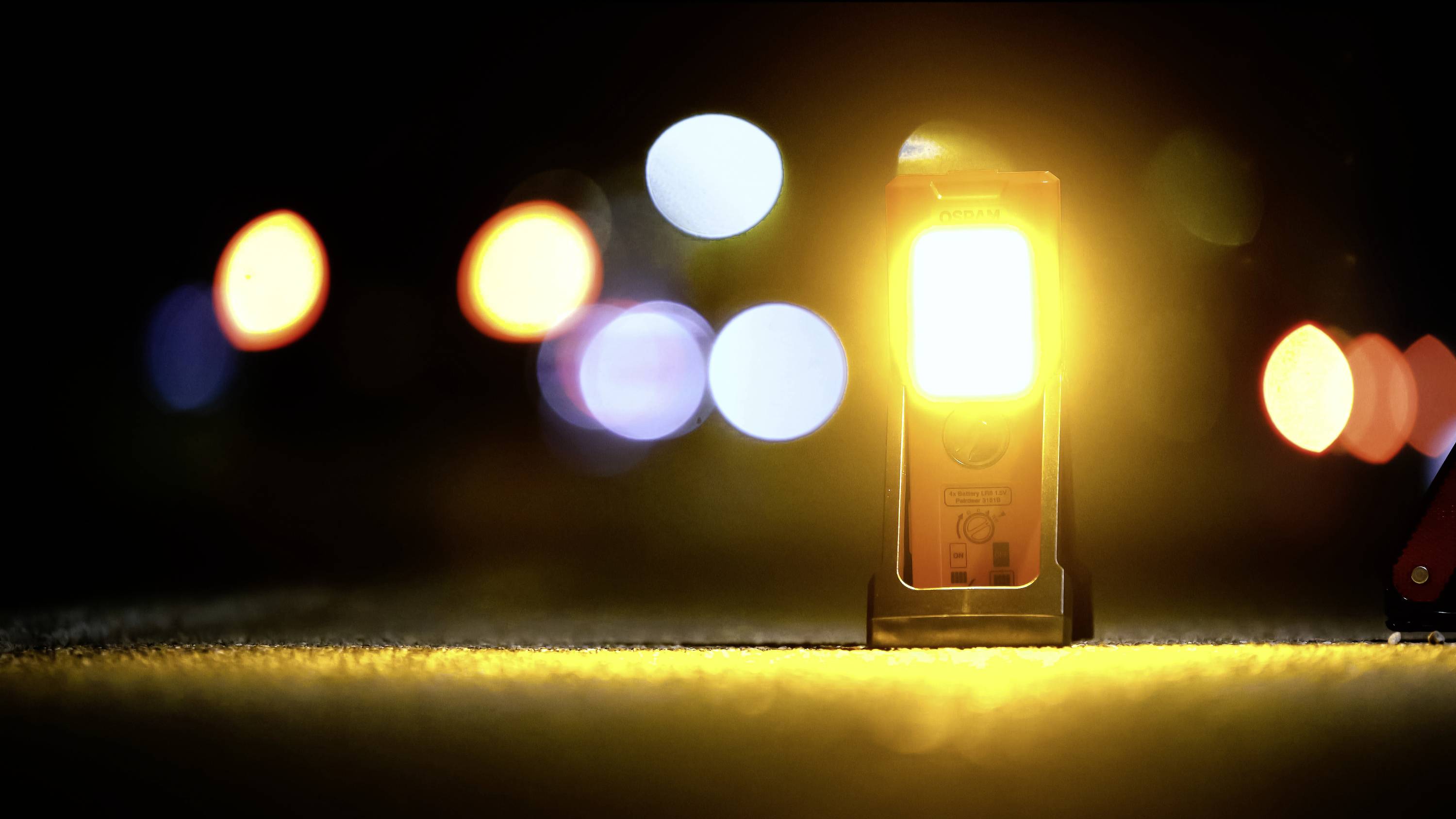 Gelbes Warnlicht leuchtet auf einer dunklen Straße, umgeben von unscharfen Lichtern im Hintergrund. Sicherheitshinweis bei Nacht.