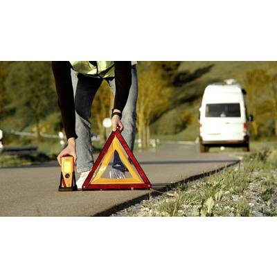 Person stellt ein Pannendreieck auf der Straße auf; im Hintergrund ein geparktes Fahrzeug. Szenario einer Autopanne oder eines Unfalls.