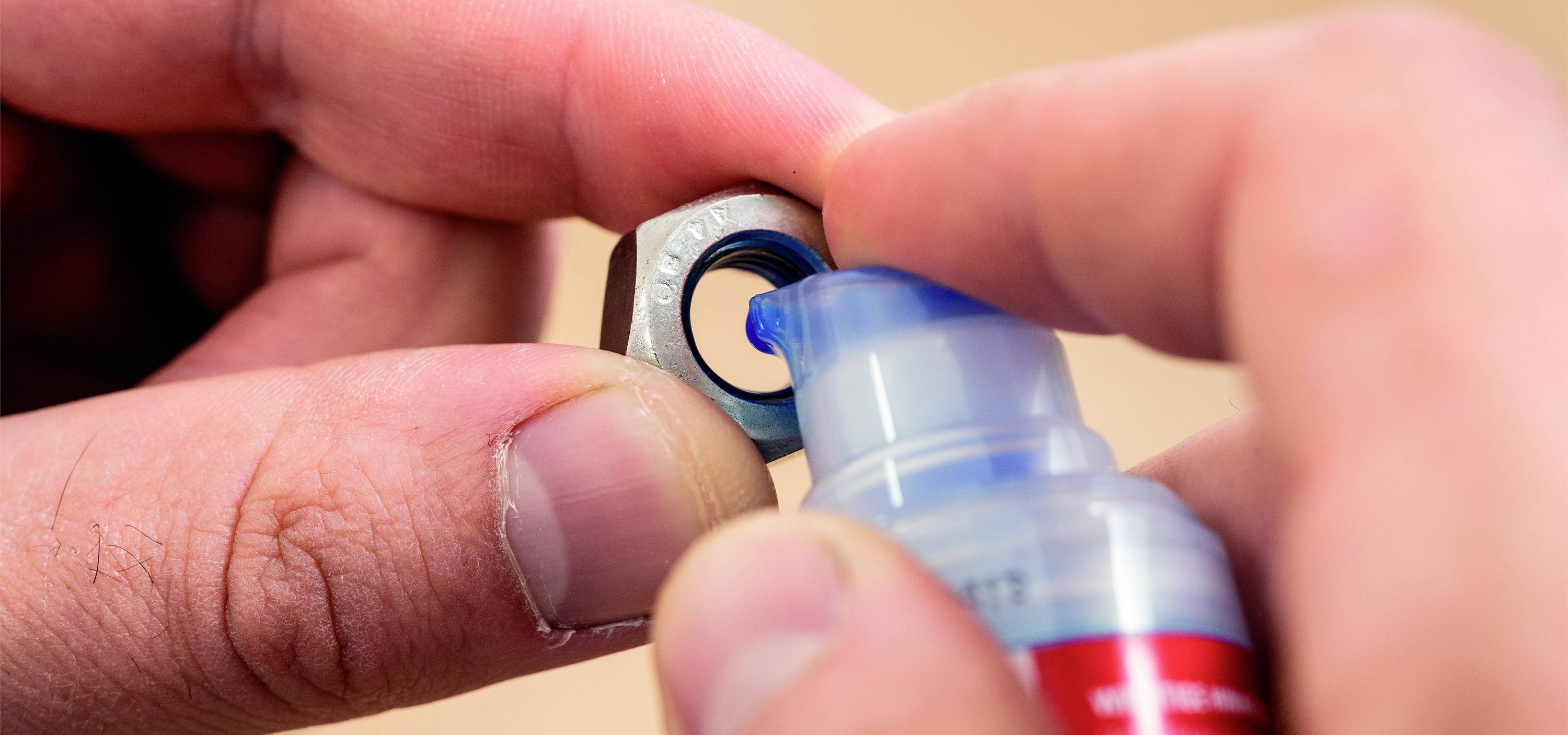 'Eine Person trägt mit einer Flasche blaue Schraubensicherungslösung auf eine Metallmutter auf.'