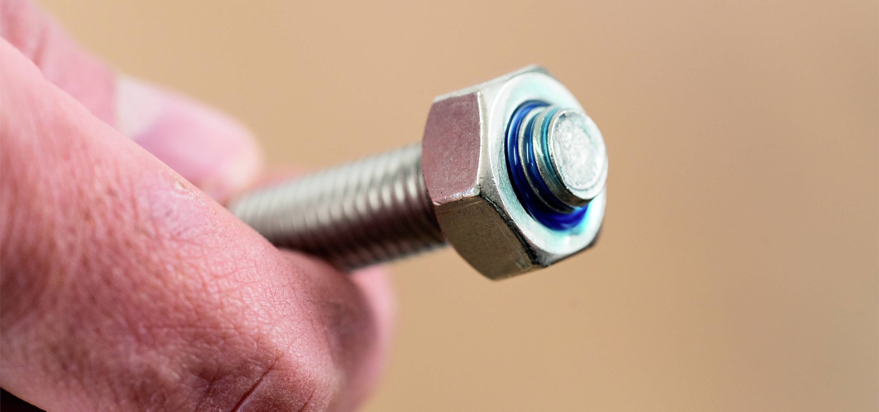 Eine Hand hält eine Metallschraube mit Mutter gegen einen unscharfen Hintergrund.