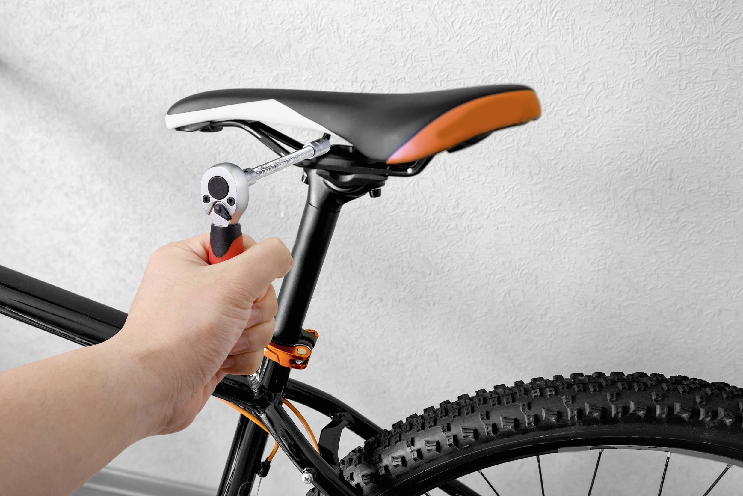 Eine Person zieht mit einem Schraubenschlüssel die Schrauben am Fahrradsattel fest. Das Fahrrad hat einen schwarzen Rahmen und grobstollige Reifen.