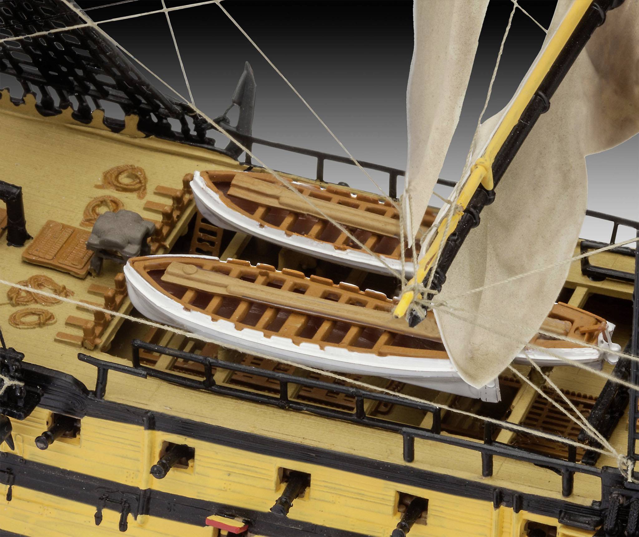 Modell eines historischen Segelschiffs mit gelber Bordwand. Zwei Rettungsboote auf Deck, umgeben von Takelage und Segeln.