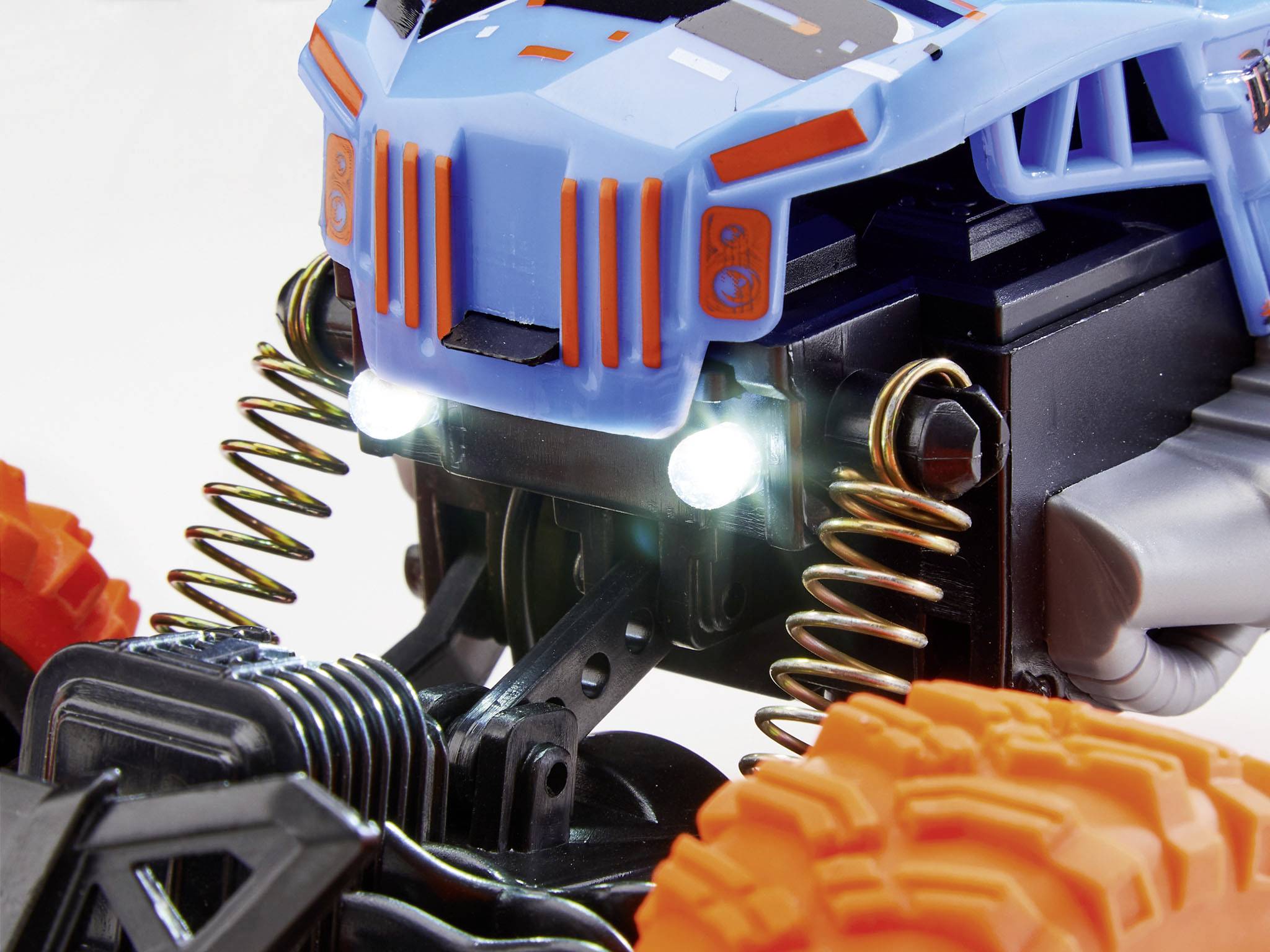 Spielzeugauto mit blauen und orangefarbenen Details. Große Spiralfedern und grobstollige Reifen sichtbar.