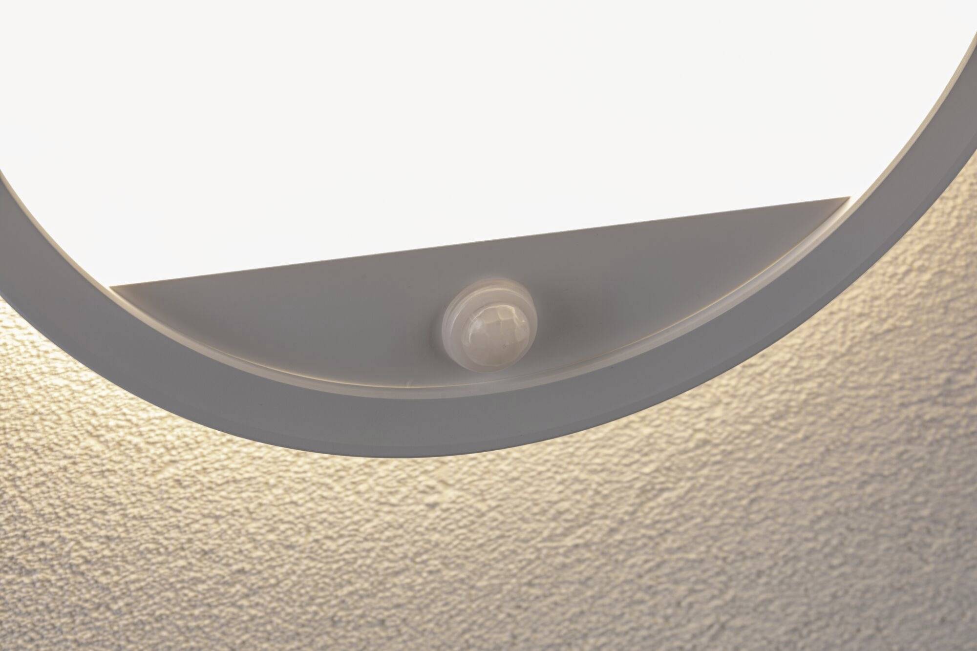 Deckenleuchte mit integriertem Bewegungssensor, montiert an einer strukturierten Decke. Die Lampe leuchtet sanft.