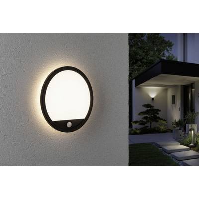 Runde Außenwandleuchte an einer Hauswand, strahlt sanftes Licht aus. Im Hintergrund ist ein beleuchteter Hauseingang und Garten zu sehen.
