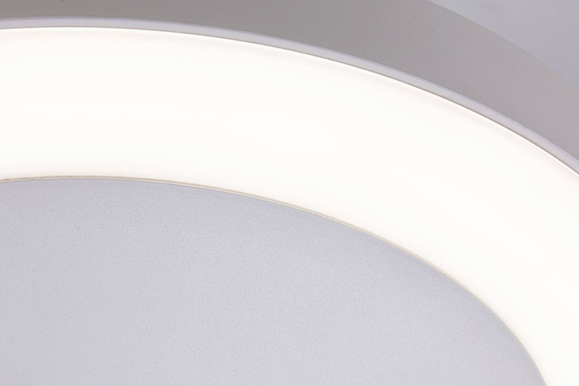 Kreisförmige Deckenlampe leuchtet hell, Detailaufnahme der weißen Lichtquelle vor grauem Hintergrund.