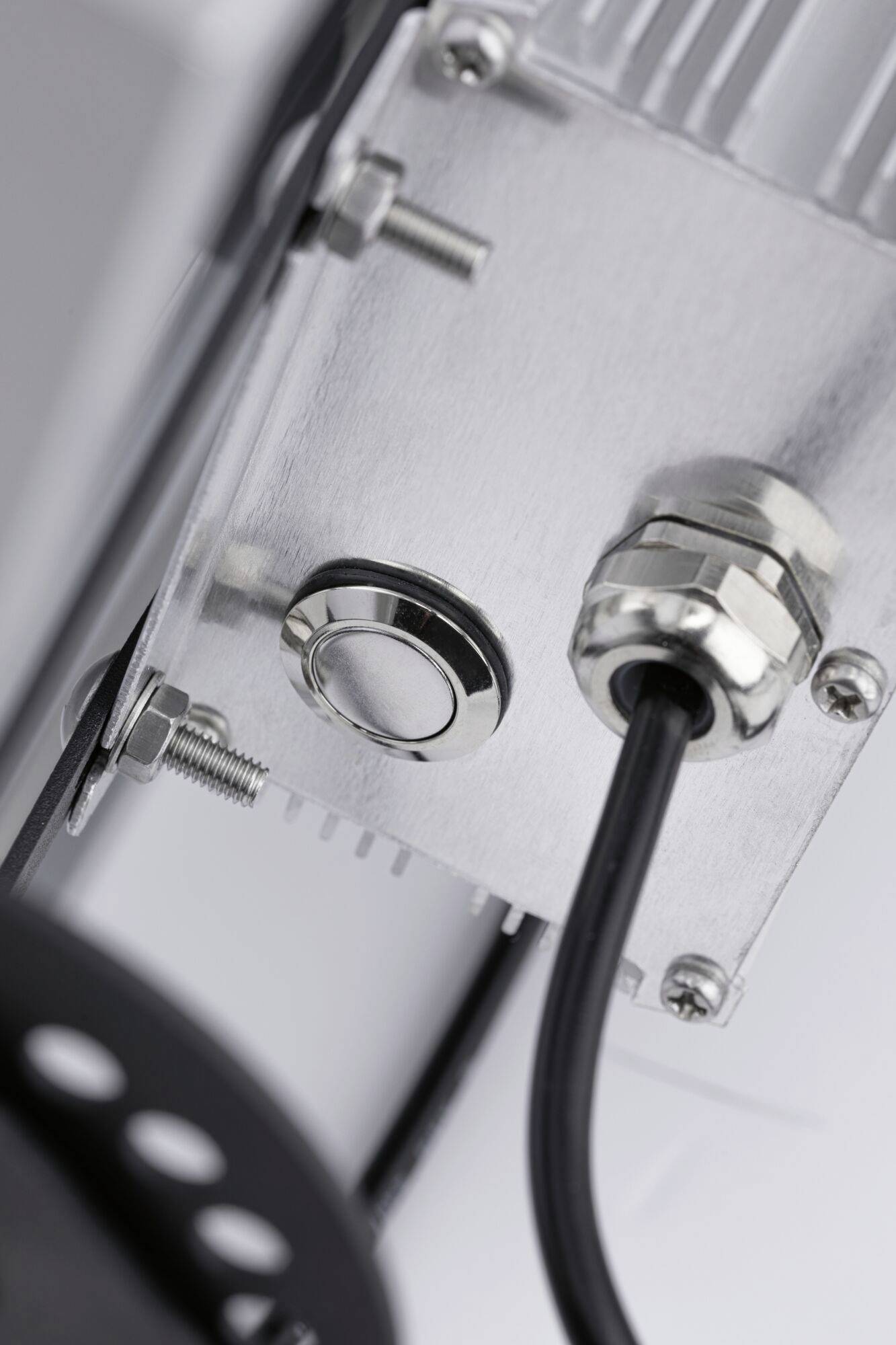 Nahaufnahme eines Metallanschlusses mit schwarzem Kabel, befestigt an einer silbernen Metallplatte mit Schrauben.