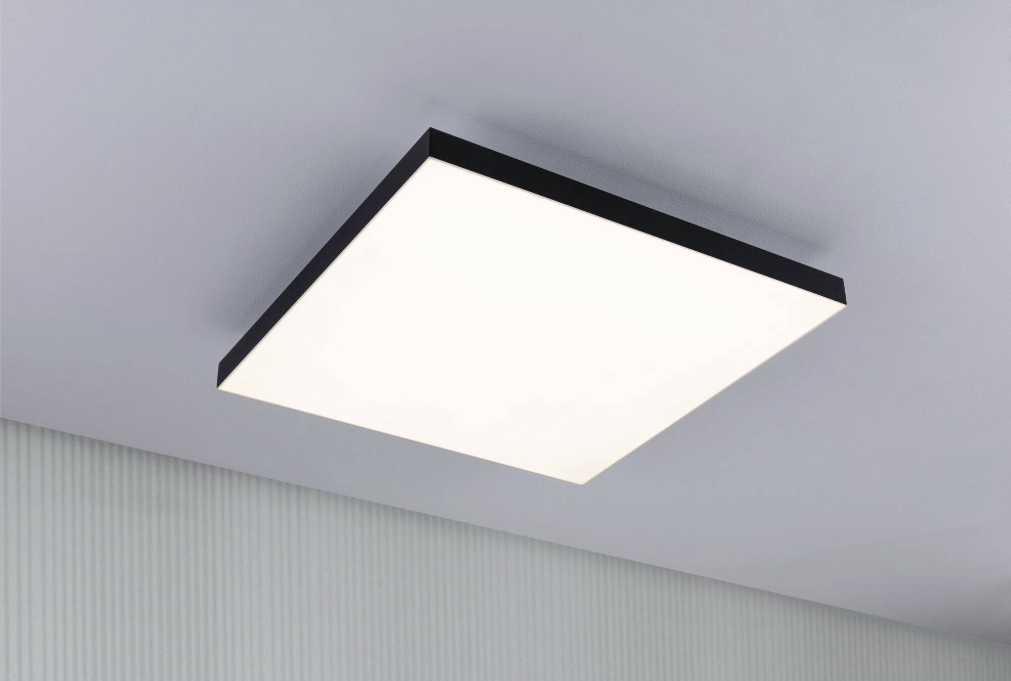 Rechteckige Deckenleuchte mit schwarzem Rahmen, die gleichmäßiges, weißes Licht in einem modernen Raum abstrahlt.