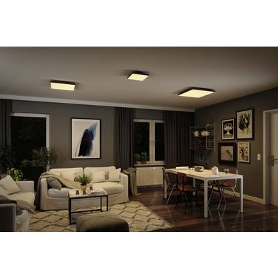 Ein modernes Wohnzimmer mit Sofa, Teppich und Esstisch. An den Wänden hängen Bilder, und von den Deckenlampen fällt warmes Licht.