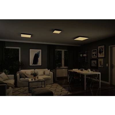Ein Wohnzimmer mit dunkler Beleuchtung. Eine Couch steht links, ein Esstisch mit vier Stühlen rechts. Kunstwerke hängen an den Wänden.