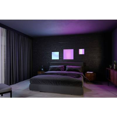Ein modernes Schlafzimmer mit einem großen Bett, dunklen Wänden und Vorhängen. An der Wand hängen drei Leuchtbilder in Blau und Rosa.