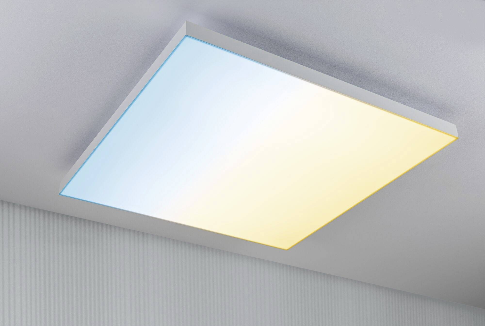 Ein rechteckiges Deckenlicht mit links blauer und rechts gelber Beleuchtung, montiert an einer grauen Decke in einem modernen Raum.
