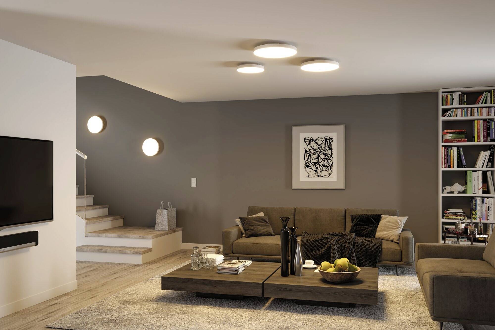 Ein modern eingerichtetes Wohnzimmer mit einem Sofa, einem Couchtisch mit Dekorationen, linken Treppen und einem Bücherregal rechts.