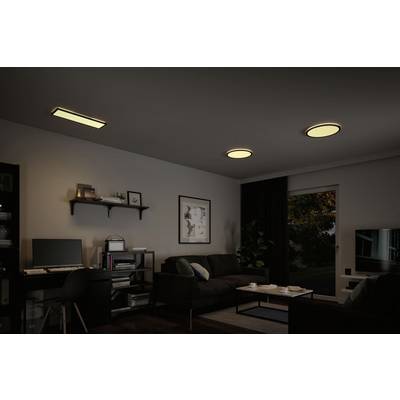 Ein modern eingerichtetes Wohnzimmer bei gedämpfter Beleuchtung. Drei Leuchten an der Decke sind eingeschaltet. Ein Sofa, ein Schreibtisch mit Computer und ein Fernseher sind zu sehen.