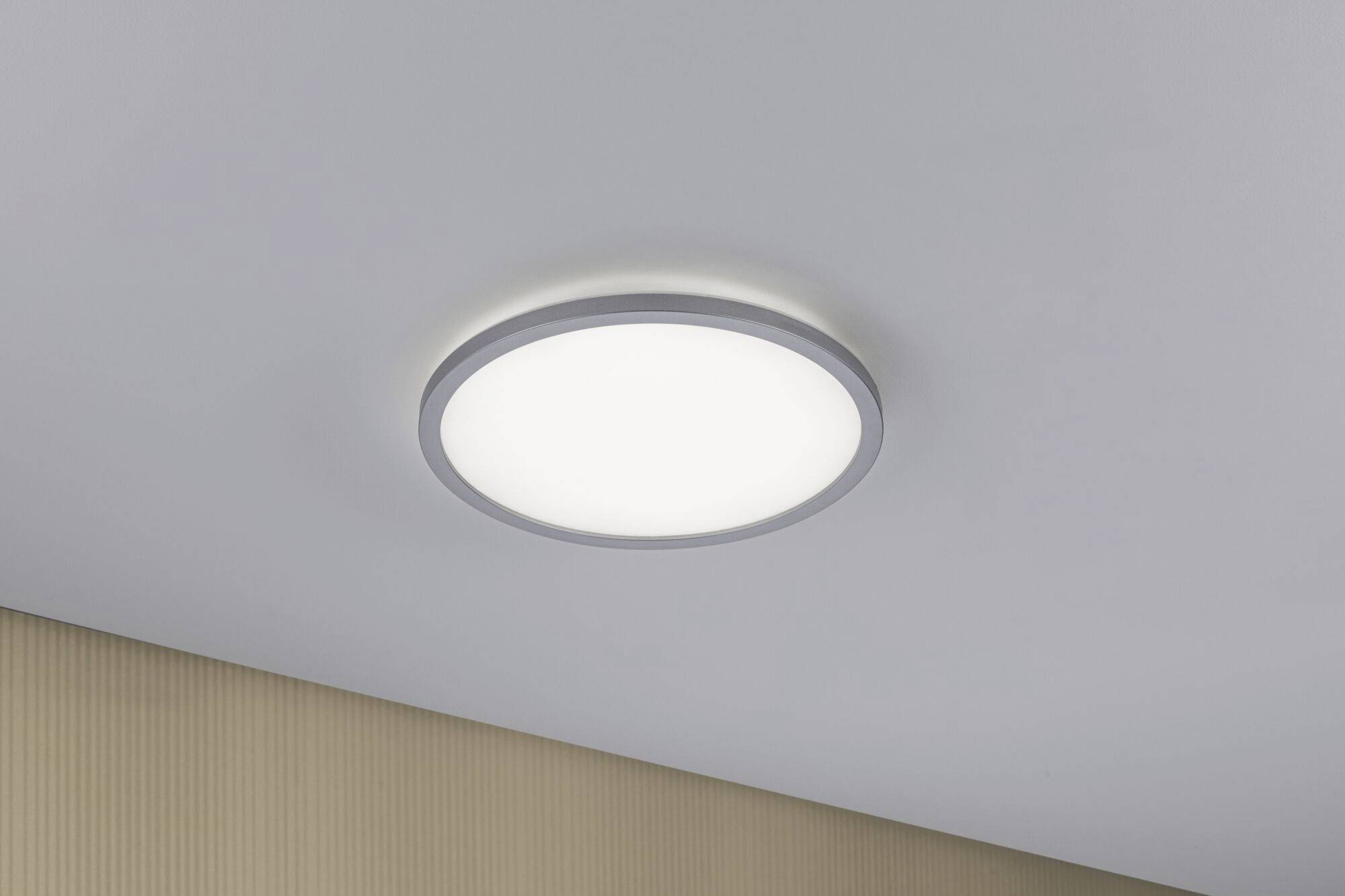 Eine runde Deckenleuchte strahlt gleichmäßiges, weiches Licht in einem modernen Raum mit beigem Akzent an der Wand aus.