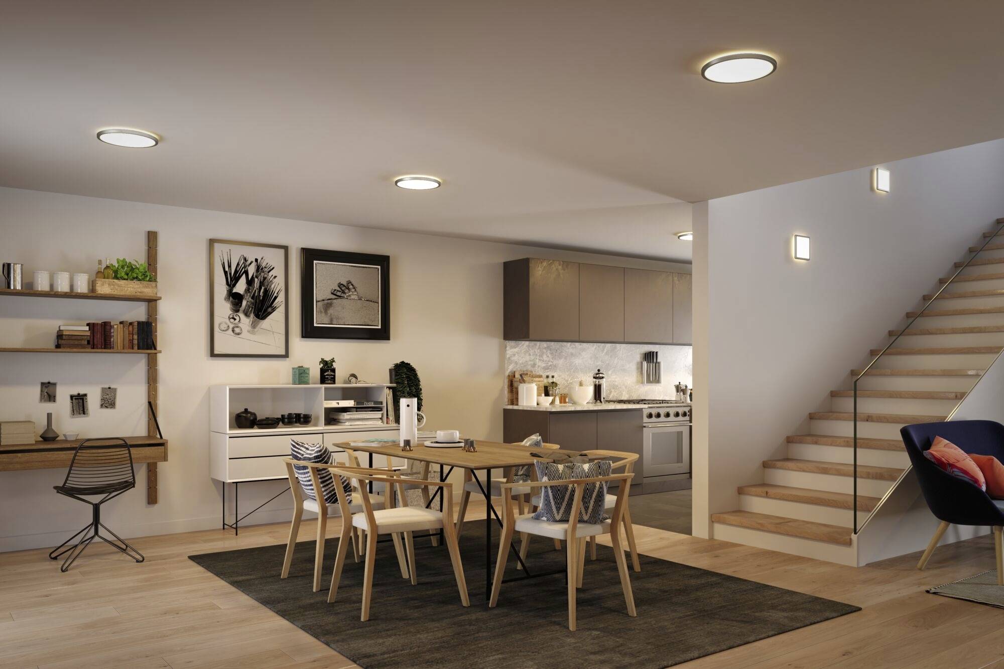 Offener Wohnbereich mit modernem Esszimmer und Küche. Ein Esstisch aus Glas mit Holzstühlen steht auf einem Teppich. Links befinden sich Regale und Bilder, rechts führt eine Treppe nach oben.