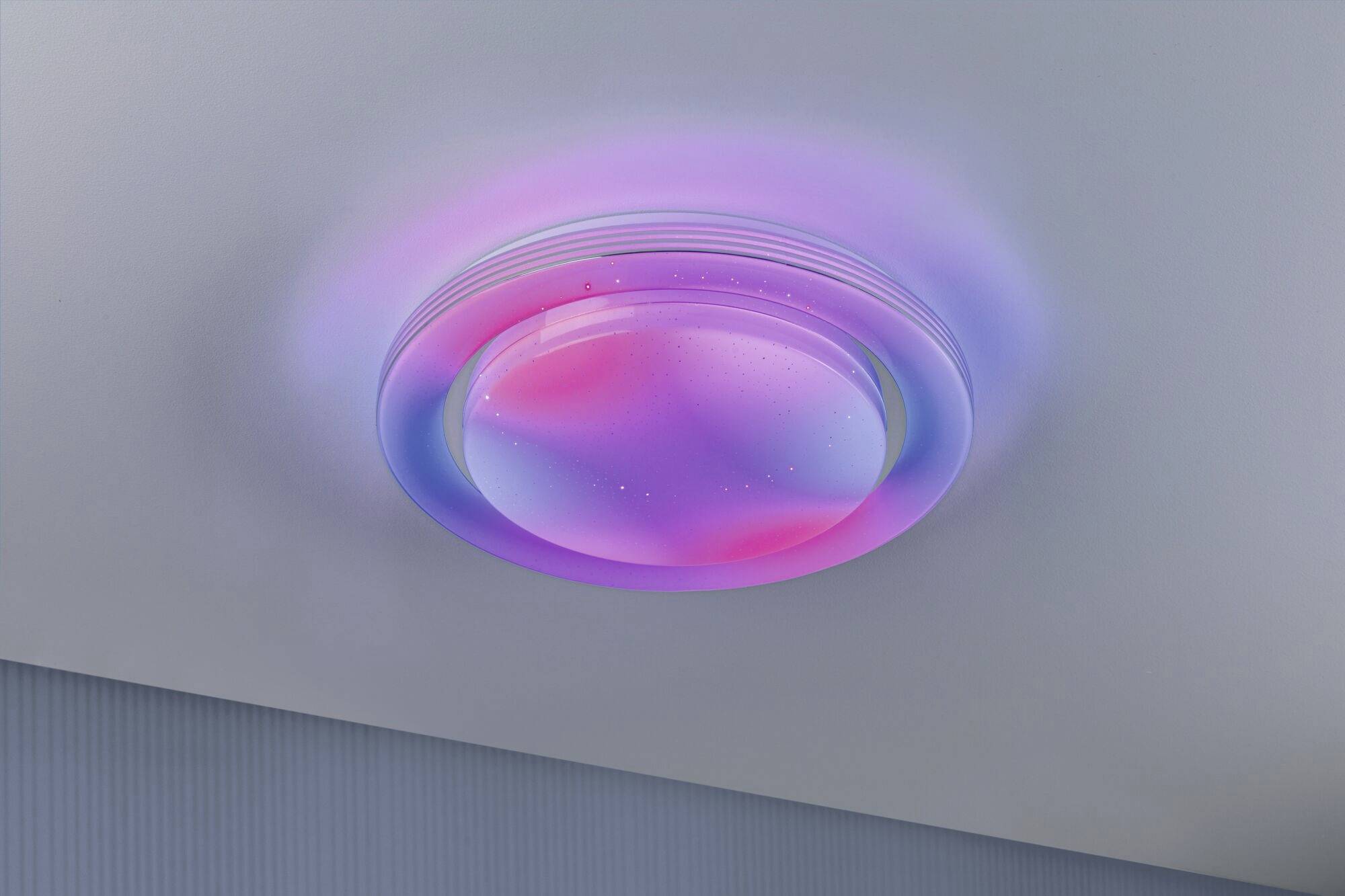 Runde Deckenleuchte mit Farbverlauf in Rosa und Blau, beleuchtet einen modernen Raum.