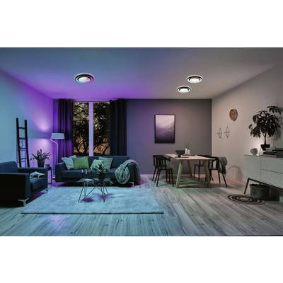 Modernes Wohnzimmer mit farbigem Stimmungslicht. Ein Sofa und Tisch gruppiert, Fenster mit Vorhang zeigt Abendhimmel.