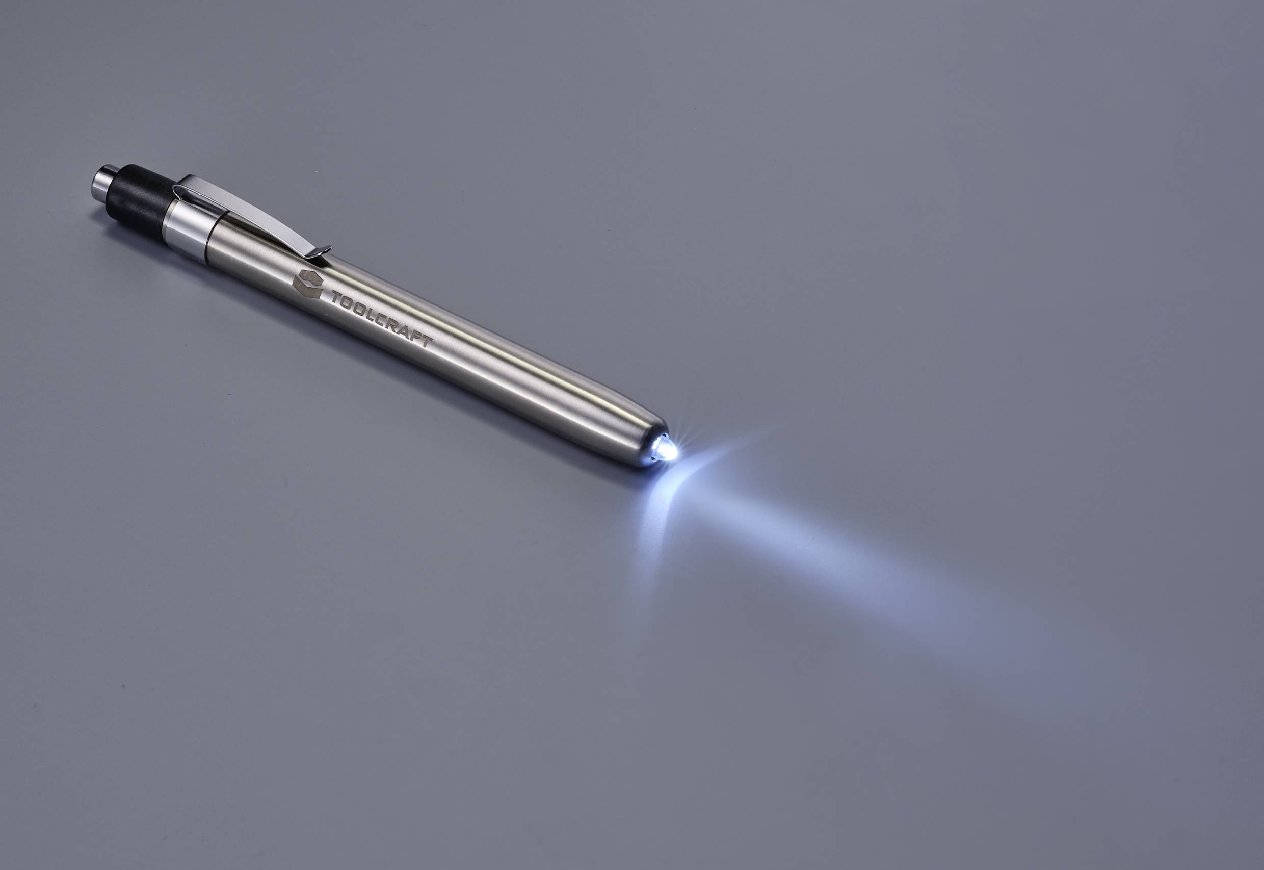 Silberner Stift-Taschenlampe auf grauer Fläche, leuchtet hell vorne.