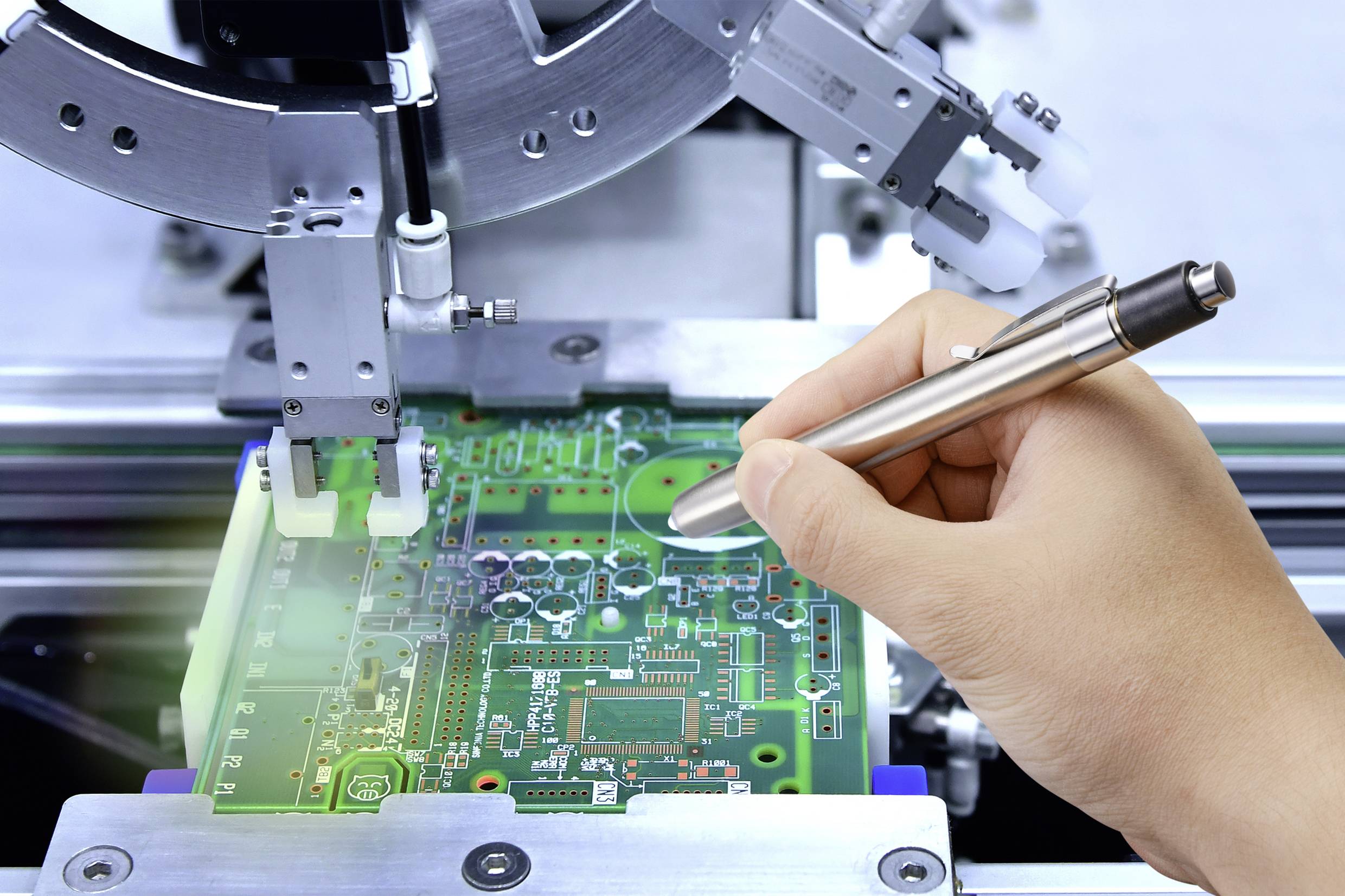 Hand prüft einen grünen Schaltkreis auf einer Leiterplatte mit einem elektronischen Gerät in einer Fertigungsumgebung.