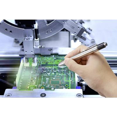 Hand prüft einen grünen Schaltkreis auf einer Leiterplatte mit einem elektronischen Gerät in einer Fertigungsumgebung.