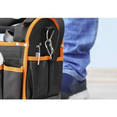 Eine schwarze Werkzeugtasche mit orangefarbenen Nähten steht auf einem Boden. Eine Person in blauen Jeans und Sneakers steht daneben.