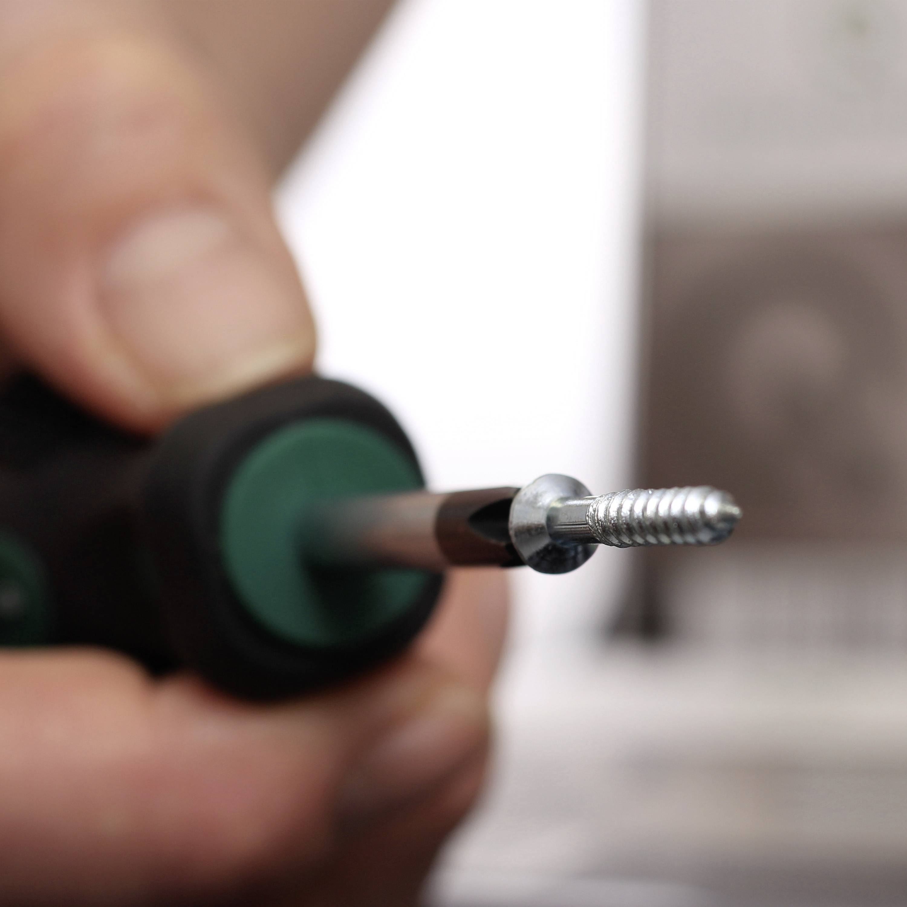 Eine Hand hält einen Schraubenzieher mit einer silbernen Schraube an der Spitze, bereit, sie in eine Oberfläche zu schrauben.