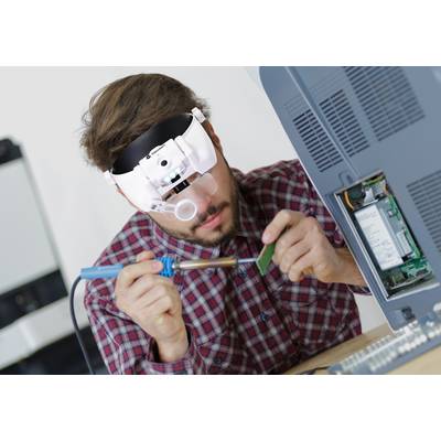 Eine Person lötet eine elektronische Platine mit einem Lötkolben, während sie eine Vergrößerungsbrille trägt.