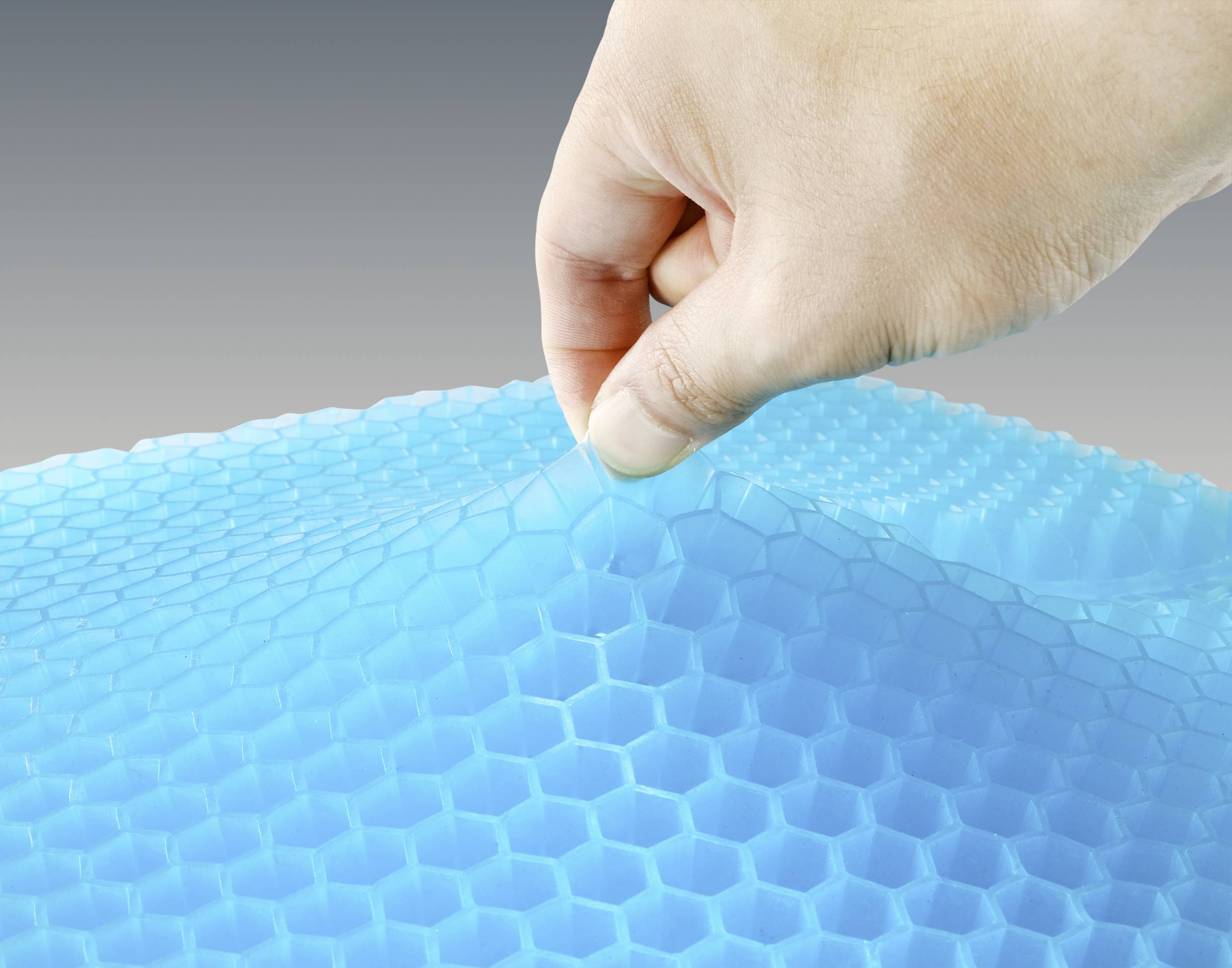 Eine Hand zieht eine Schicht von blauer Wabenstrukturfolie nach oben. Die Folie zeigt hexagonale Muster und sieht leicht flexibel aus.