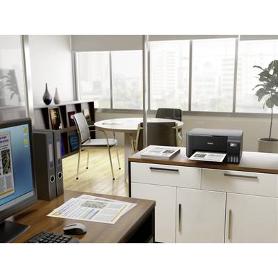 Ein modernes Büro mit hellem Tageslicht, Schreibtisch mit Computer und Drucker, runder Tisch im Hintergrund, große Fenster zeigen Stadtblick.