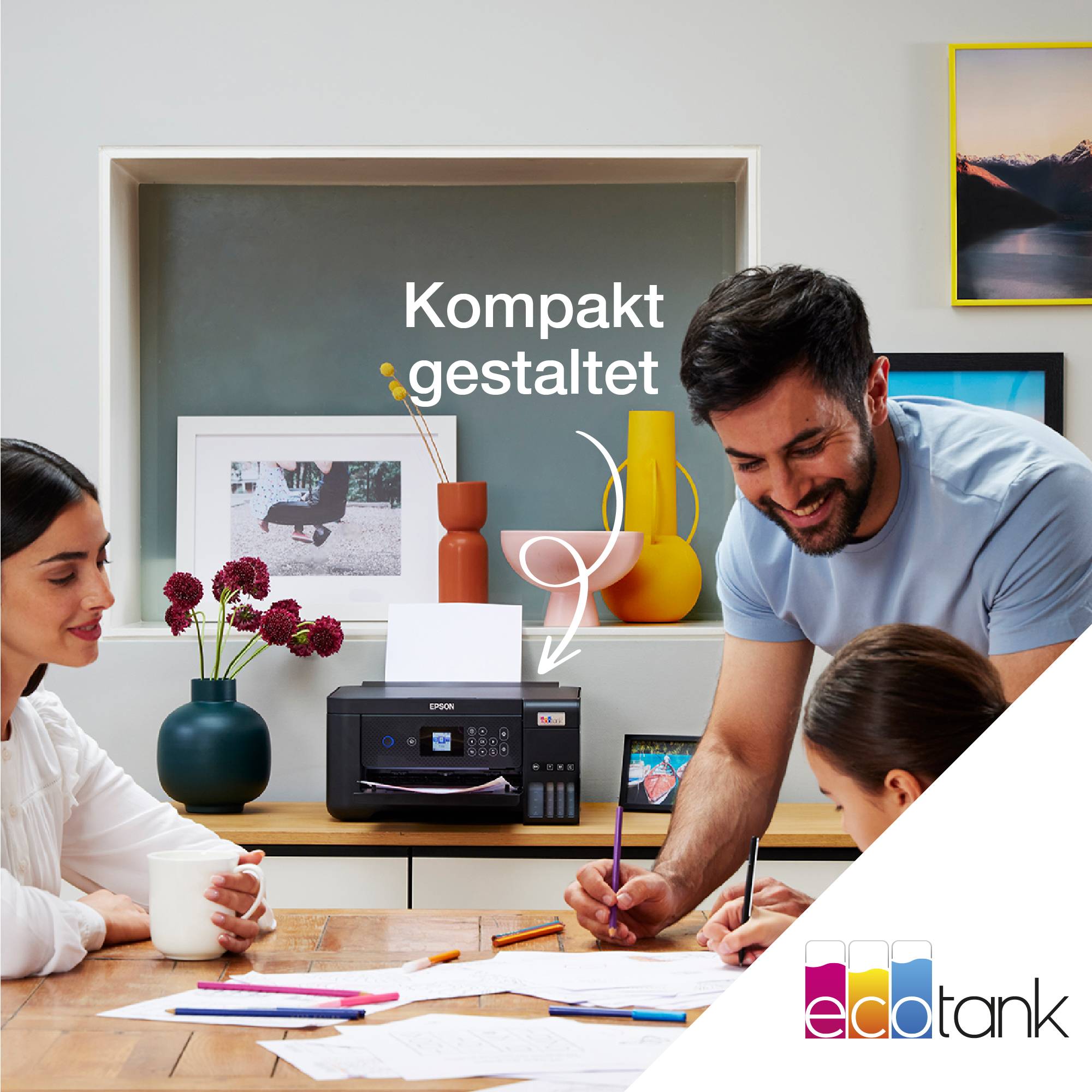 Eine Familie sitzt um einen Tisch. Ein Drucker steht im Mittelpunkt, der als „kompakt gestaltet“ beschrieben wird. Im Hintergrund stehen dekorative Objekte.