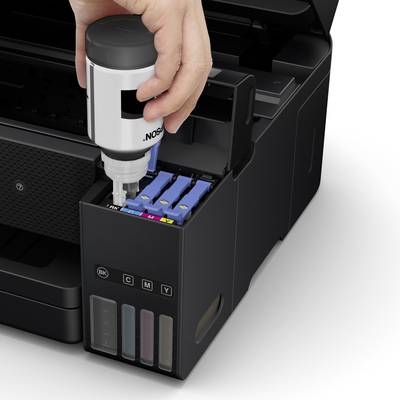 Eine Hand füllt schwarze Tinte in einen Druckertank nach. Der Drucker hat separate Fächer für Schwarz, Cyan, Magenta und Gelb.