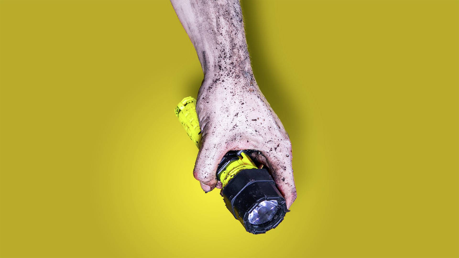 'Eine schmutzige Hand hält eine gelbe Taschenlampe vor einem einfarbig gelben Hintergrund.'