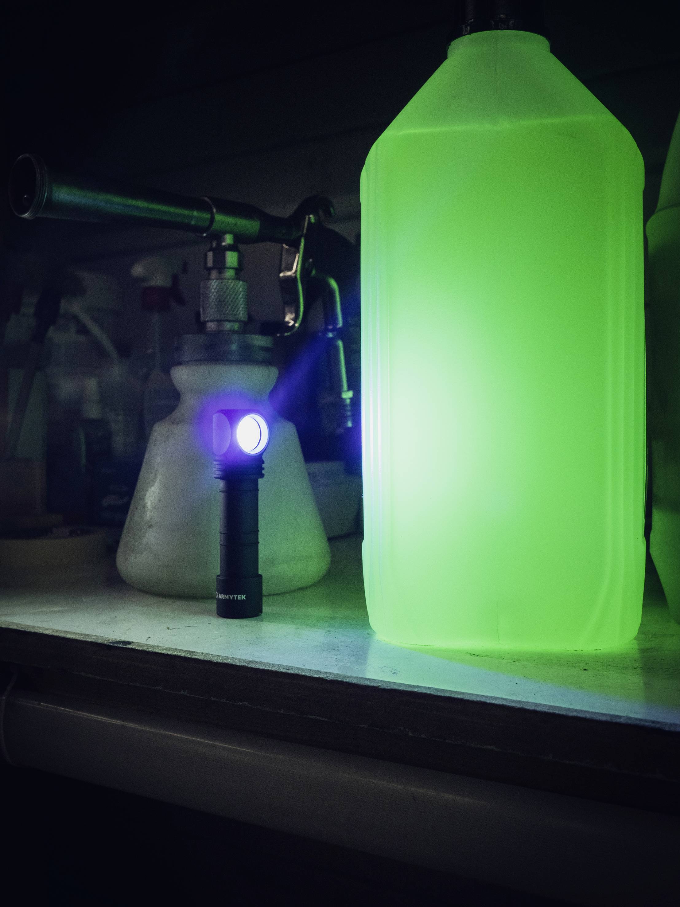 Taschenlampe beleuchtet grüne Flüssigkeit in einer Flasche, chemische Laborutensilien im Hintergrund, dunkle Umgebung.