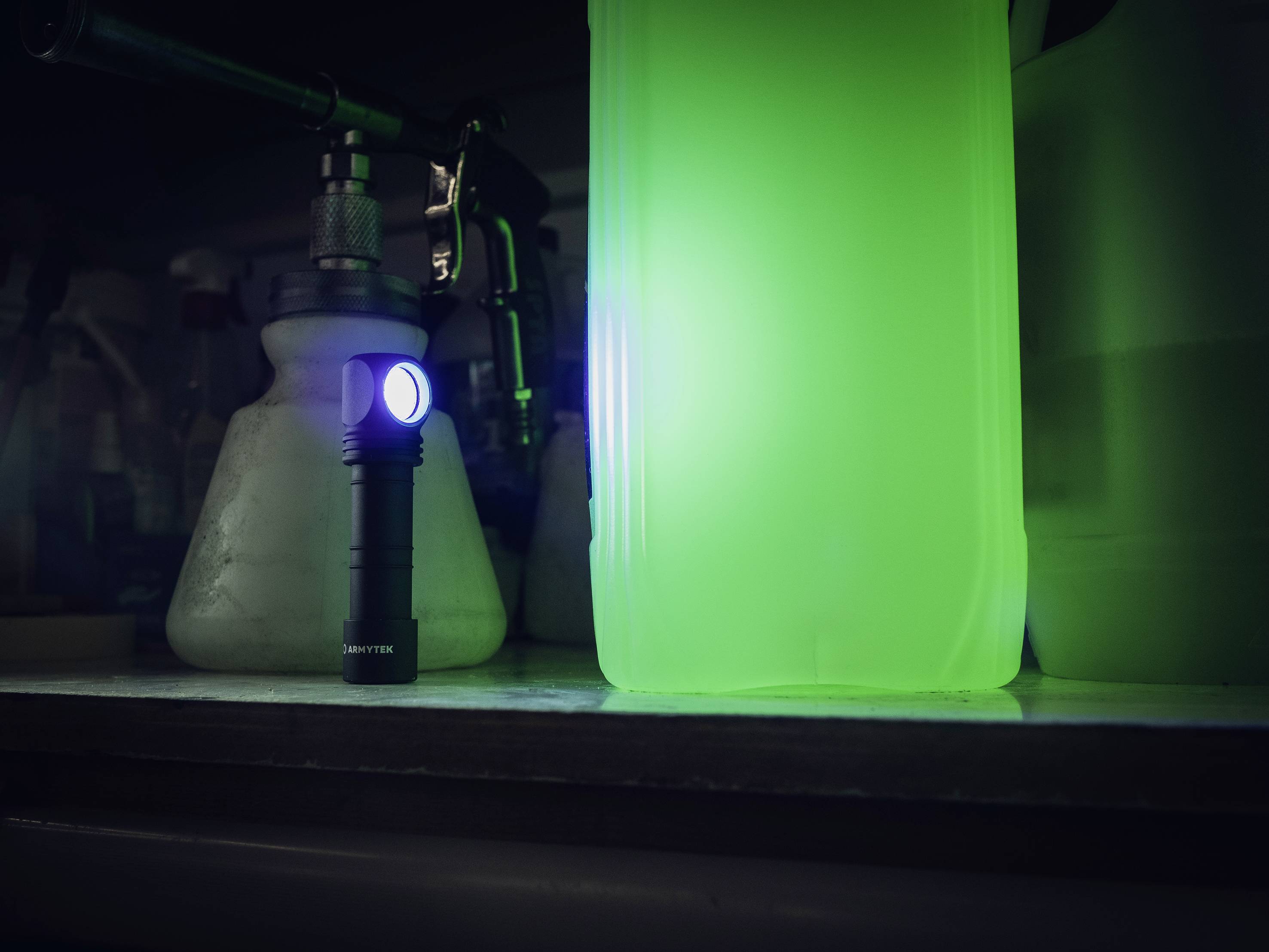 Eine leuchtende Taschenlampe auf einem Regal neben einem großen, grün strahlenden Kanister in einer dunklen Umgebung.