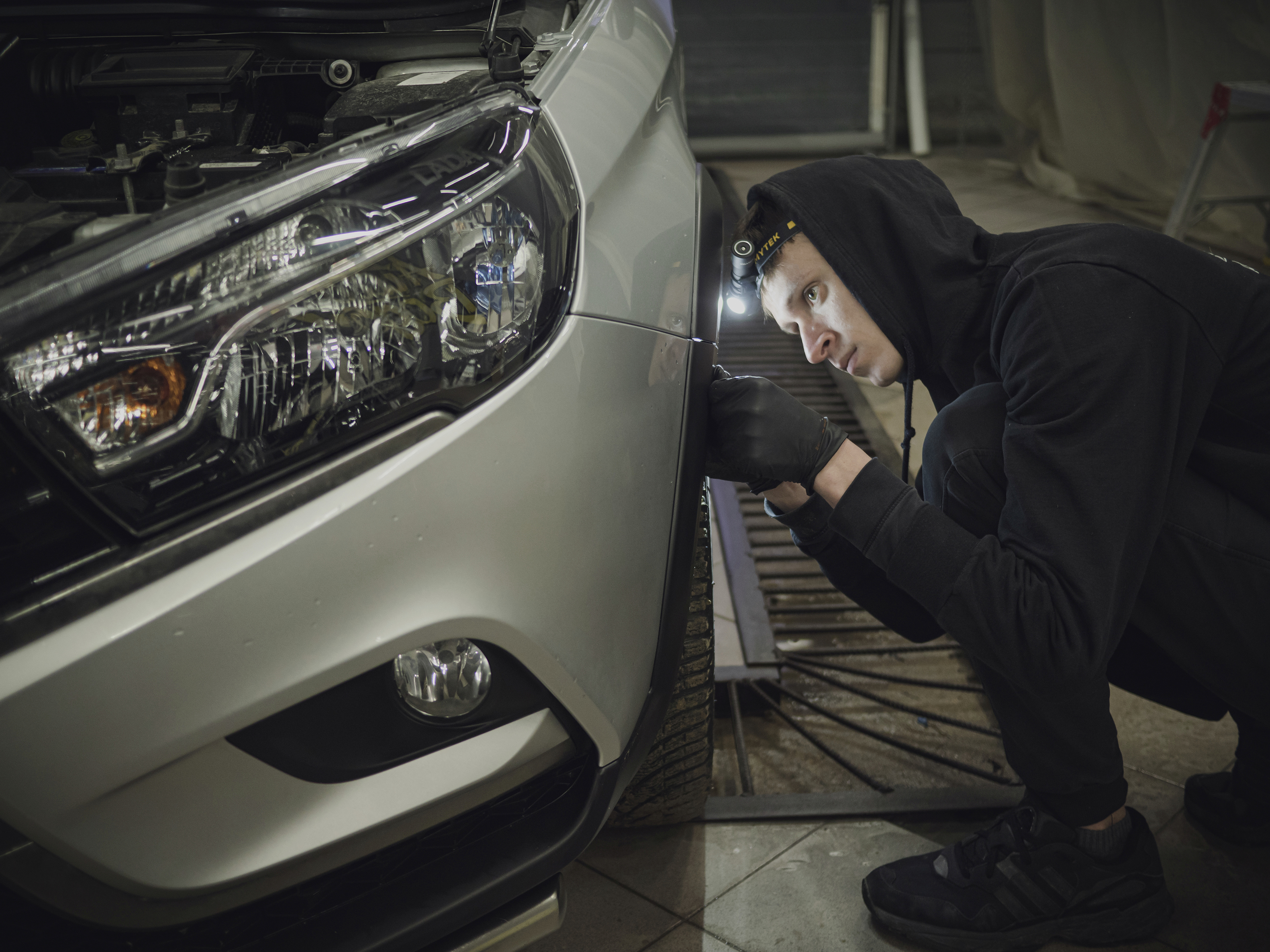 Eine Person in Arbeitskleidung inspiziert aufmerksam den rechten Vorderreifen eines Autos in einer Werkstatt.