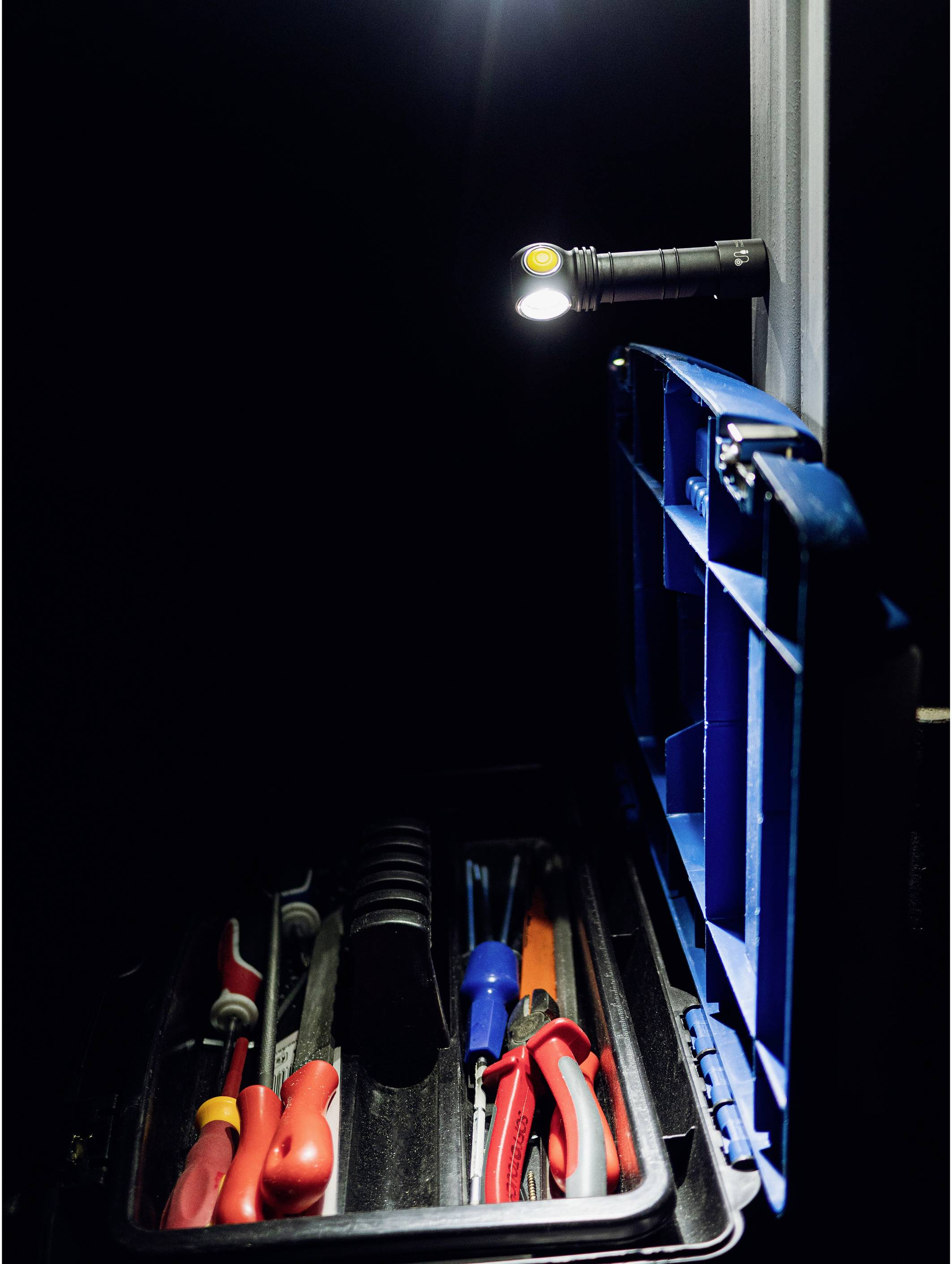 Eine geöffnete blaue Werkzeugkiste mit verschiedenen Werkzeugen innen. Eine kleine Lampe beleuchtet den Inhalt im Dunkeln.