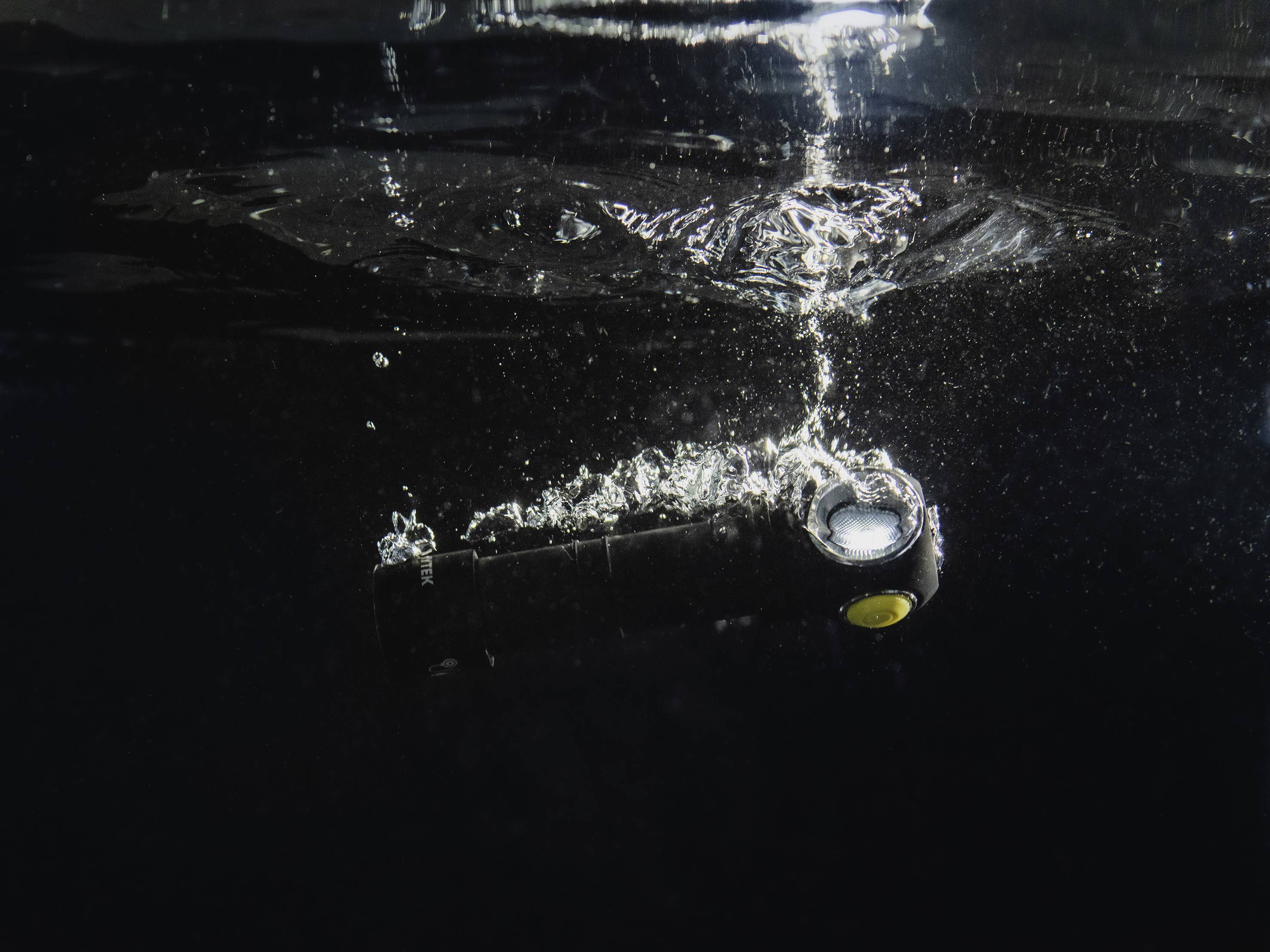 Eine Taschenlampe unter Wasser, von Blasen umgeben, die nach oben steigen. Die Szene zeigt einen Tauchgang oder Test der Wasserfestigkeit.