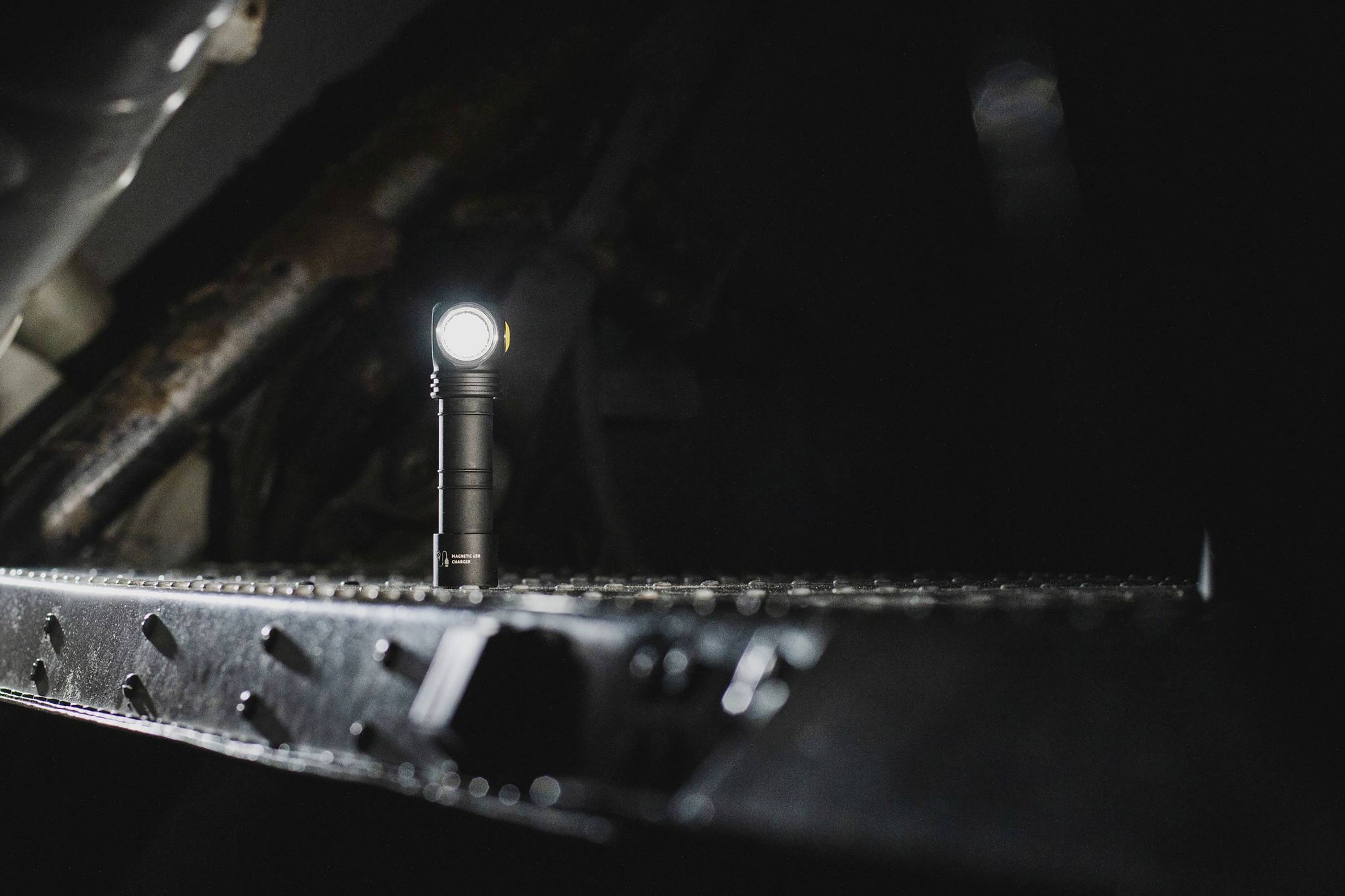 Eine Taschenlampe leuchtet in einem dunklen Raum, platziert auf einer metallischen Oberfläche mit Nieten, die auch im Dunkeln sichtbar sind.