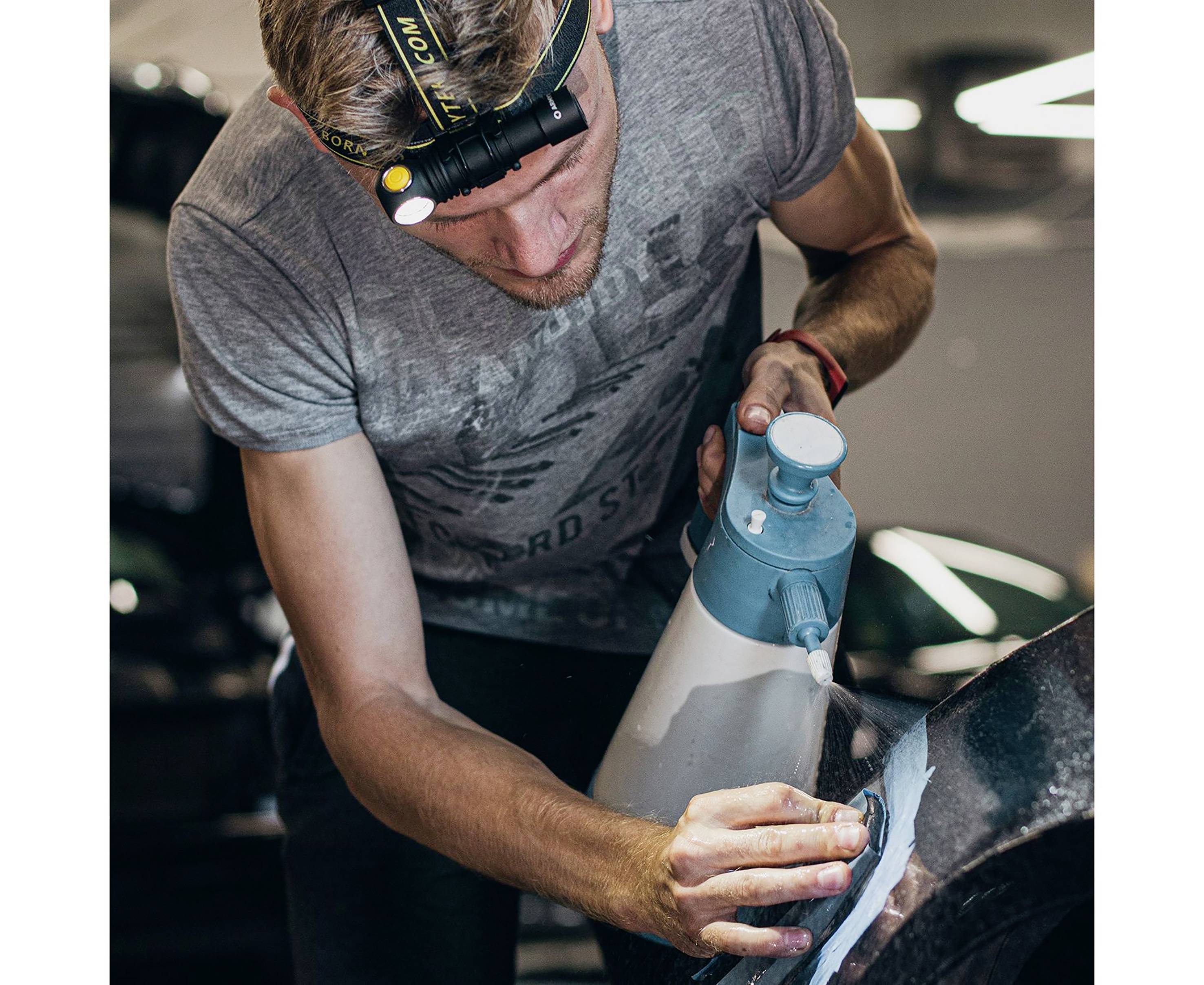 Eine Person poliert mit einer Maschine die Oberfläche eines Autos in einer Werkstatt. Sie trägt ein Stirnlicht für bessere Sicht.